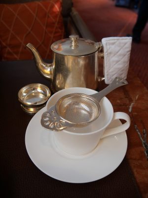 A cup of peppermint tea served with a teapot and strainer